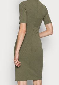 Robe côtelée vert olive à la silhouette ajustée, manches courtes et col montant, avec une texture subtile et des détails de couture.