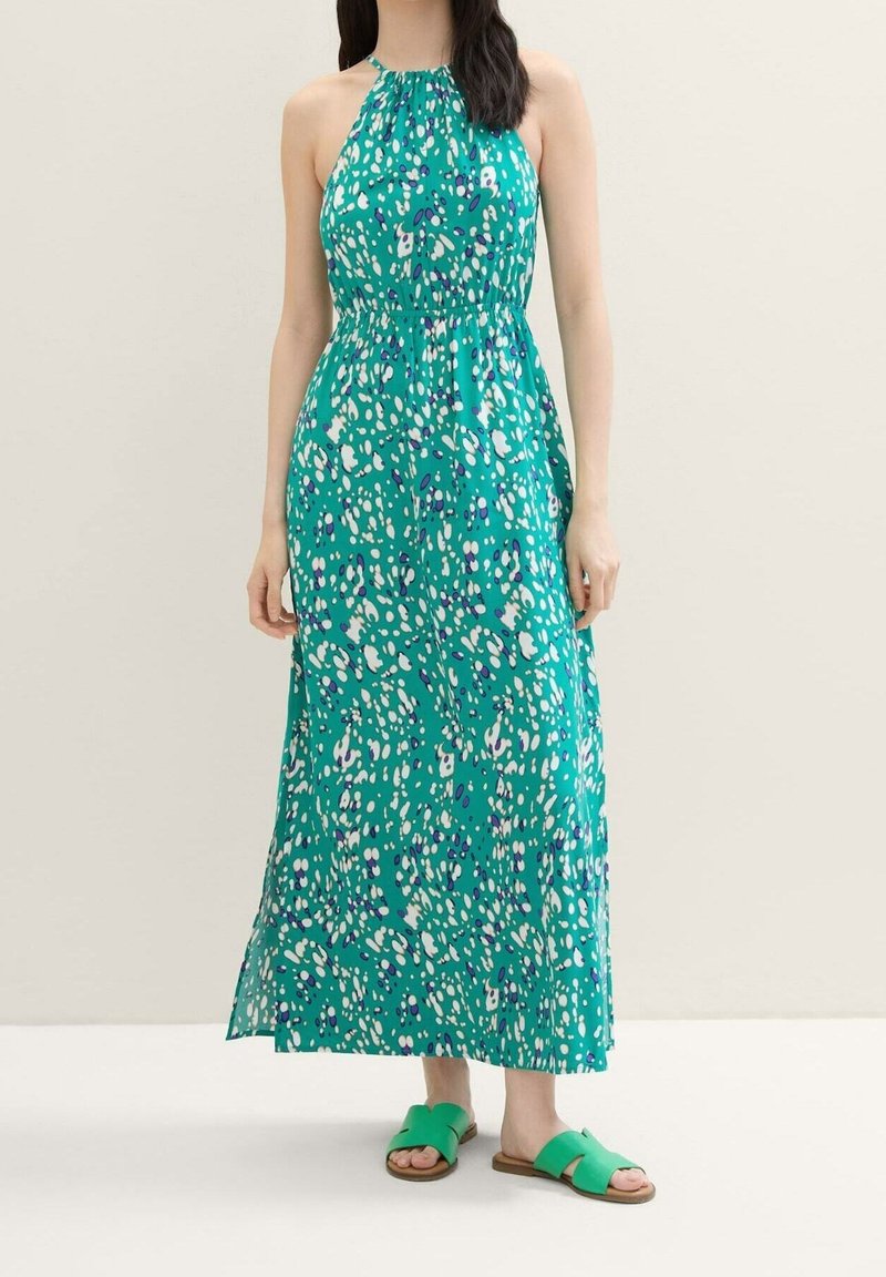 Abito maxi con scollo all'americana in turchese con macchie astratte bianche e viola. Tessuto leggero, fascia elastica in vita, orlo a strati. Sandali piatti verdi.
