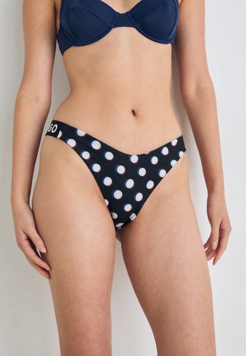 Fekete bikini alsó fehér és piros pöttyökkel. Alacsony üléssel és márkás derékpánttal rendelkezik. Simává textúra, formázott kivitel.