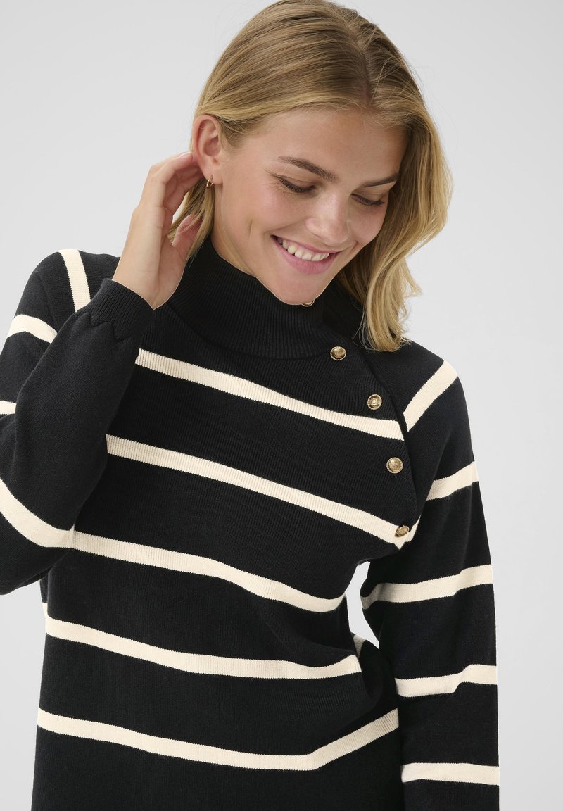 Gestreifter Pullover in Schwarz und Weiß mit hohem Kragen und goldenen Knopfakzenten an der Schulter. Weiches Strickmaterial mit lockerer Passform.
