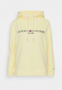 Sudadera de algodón amarilla con capucha ajustable, que presenta un logo frontal "TOMMY HILFIGER EST. 1985" en color marino y rojo. Puños y dobladillo de canalé.