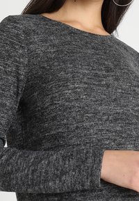 Šedé texturované dlouhý rukáv s širokým výstřihem. Látka má jemný melírovaný vzor, žebrované manžety a přiléhavý střih.