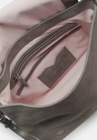 Innenraum einer grauen Wildlederhandtasche mit hellrosa Futter. Verfügt über ein Reißverschlusstäschchen und eine kleine flache Tasche mit Etikett. Glatte Textur, schlichtes Design.