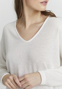 Lichte beige, loszittende V-hals trui van gebreid materiaal met een gestructureerd oppervlak. Voorzien van lange mouwen en geribbelde manchetten.