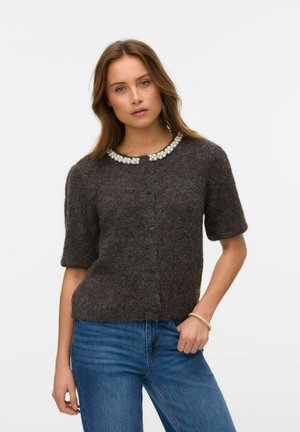 Korte mouwen, kegelgrijze cardigan gemaakt van een zachte wolmix, met een parelcollar en een knoopsluiting aan de voorkant. De spijkerbroek is middelblauw.