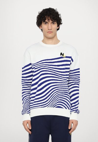 Pull en maille blanche avec des rayures ondulées bleues, des poignets et un bas côtelés, arborant un petit logo noir et jaune sur la poitrine.