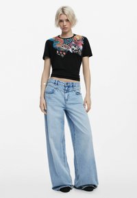 Black cropped t-shirt with colorful floral graphic and light blue wide-leg jeans. The outfit features a high waist and subtle whiskering.