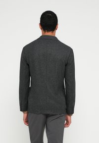 Blazer cinzento em tweed com lapela de entalhe, abertura simples e três botões nas mangas. Apresenta um corte ajustado e tecido texturizado.