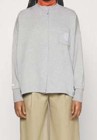 Grå, knap-up sweatshirt med hög krage, sidofickor och en ficka på vänster bröst. Mjuk tyg, avslappnad passform, ribbade ärmslut.