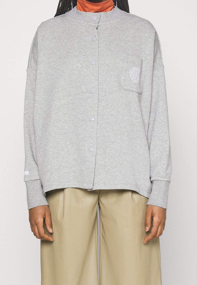 Grå, knap-up sweatshirt med hög krage, sidofickor och en ficka på vänster bröst. Mjuk tyg, avslappnad passform, ribbade ärmslut.