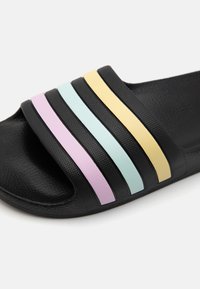 Schwarze Slide-Sandale mit drei horizontalen bunten Streifen in Pastelltönen: Lavendel, hellblau und gelb. Strukturiertes Material.