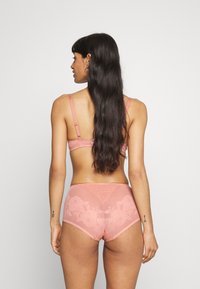 Completo di lingerie rosa con reggiseno a pizzo sul retro e culotte alte abbinate con ricami floreali e bordi smerlati. Materia morbida e liscia.