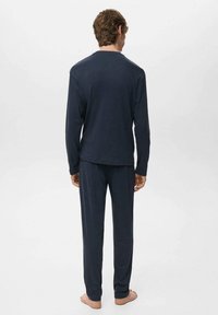 Navyblaues Loungewear-Set aus strukturiertem Stoff; besteht aus einem langärmligen Oberteil und einer Hose, die gerade geschnitten und locker geschnitten sind.