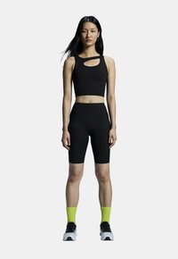 Must olla must crop top lõikega, mis on kombineeritud kõrge vöökohaga mustade lühikestega. Kandmine on täiustatud erekollaste soonikkudede sokkidega ja sportlike mustade kingadega.