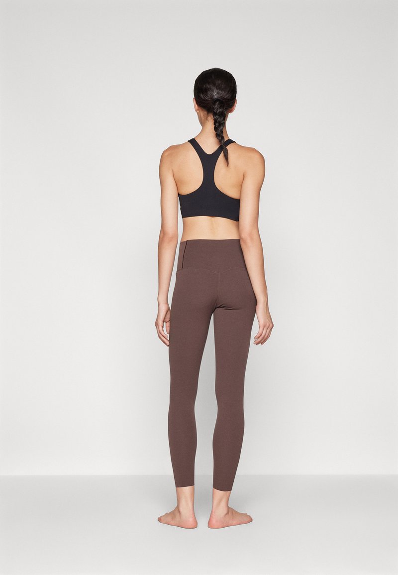 Zwarte sportbh met een racerback ontwerp, gecombineerd met bruine high-waisted leggings met een strakke, gladde textuur en subtiele stiksels.
