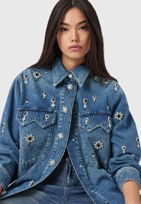 Tumesinise teksajakk, mis on kaunistatud hõbedaste ja mustade lillemotiividega aplikaatide ning väikeste naelakestega. Klassikalise krae ja nööpkinnitusega.