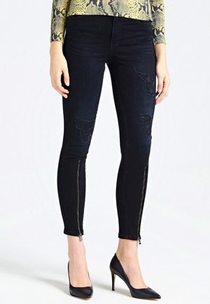 Slimme jeans van donkere denim met versleten details en ritsen bij de enkels, gecombineerd met zwarte hoge hakken.