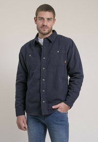 Chemise bleu marine à boutons en tissu doux, dotée de deux poches sur la poitrine avec rabat et fermeture à bouton, à manches longues et col classique.