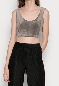 Szary aksamitny crop top z szerokim dekoltem w serek i bez rękawów, zestawiony z czarnymi, fakturowanymi spodniami z wysokim stanem.