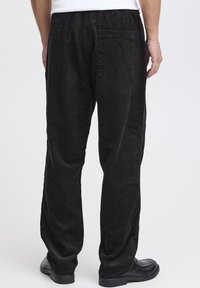 Pantaloni in velluto nero a coste con vestibilità comoda, dotati di tasca posteriore e motivo a coste testurizzato. Abbinati a scarpe nere.