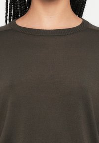 Rudas megztinis su apvalia apykakle ir ribinėmis kraštelėmis. Turi lygią tekstūrą ir aptemptą dizainą, tinkantį kasdieniam dėvėjimui.