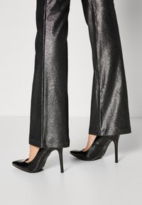 Zwarte patenten leren hoge hakken met een spitse neus en stilettohak. Gecombineerd met glanzende zwarte flared broeken met een strakke textuur.