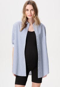 Gestreiftes Button-Up-Hemd in Blau und Weiß, leichtes Material, Kragen und kurze Ärmel, getragen über einem schwarzen Tanktop und Shorts.