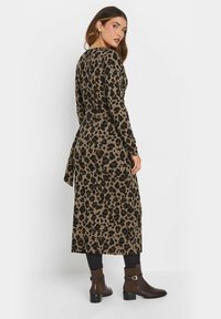 Pitkähihainen leopardikuosisnistukävelydressi, jossa on solmittava vyötärö ja pehmeä kangas. Yhdistetty ruskeisiin nilkkureihin ja mustiin legginsseihin.
