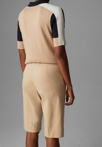 Polo shirt in maglia di colore beige con dettagli a pannello in navy e bianco, abbinato a pantaloni corti beige che raggiungono la metà della coscia, design minimalista, texture morbida.