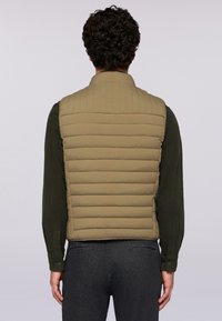 Béžová prošívaná vesta s vysokým límcem, texturovanou látkou a přiléhavým střihem, nošená přes tmavé tričko, se hladkým zadním dílem a bez viditelného kovového zapínání.