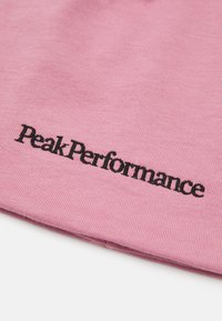 Pink fabric with ribbed texture displaying the embroidered black text "Peak Performance" prominently.