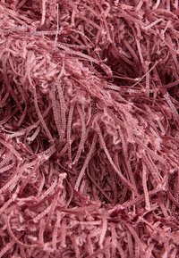 Primo piano di fili di filato rosa polveroso attorcigliati, con una trama mista di anelli lisci e fibre soffici intrecciate.