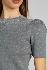Szary sweter z krótkim rękawem i okrągłym dekoltem, z teksturowanej tkaniny z małymi zdobieniami w górnej części.