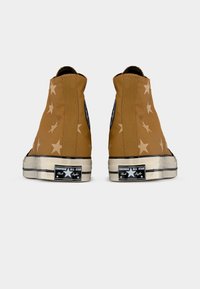 Pruunid kõrgete säärega Converse tossud beežide tähemustritega, kulunud välimise kontsaga nähtavate must-valgete "Converse All Star" logodega.