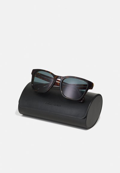 Ochelari de soare cu rame din fâșii de țestoasă și lentile întunecate, așezați pe un capac cilindric din piele neagră, cu însemnătatea "Giorgio Armani".
