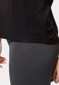 Camicetta nera a maniche corte con una texture liscia e orlo cucito; presenta un logo ricamato "LES LUNES" vicino al fondo. Leggings grigi con texture a coste.