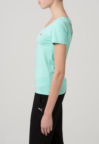 Jasnozielony sportowy t-shirt z okrągłym dekoltem, krótkimi rękawami i wycięciem z tyłu, zestawiony z czarnymi spodniami dresowymi z logo.