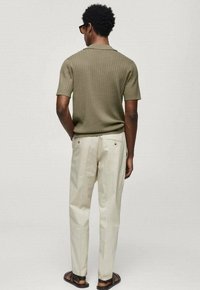 Oliivivärviline ribadega lühikeste varrukatega särk, beežid püksid, mustad sandaalid; sile kudum, lõdva istuvusega, tagantvaade jääb fookusesse disaini detailidega.