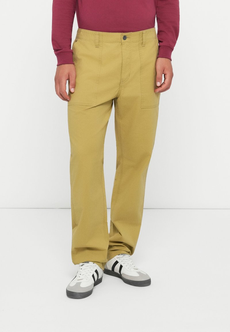 Khaki katoenen broeken met een relaxte pasvorm, voorzien van zijzakken en een knoopsluiting. Gepaard met wit en grijs sneakers.
