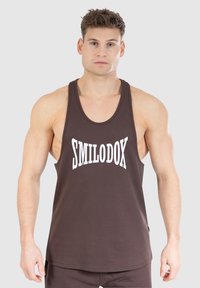 Brązowy, bezrękawnik wykonany z bawełny, z białym napisem "SMILODOX" na klatce piersiowej. Gładka textura, luźny krój.