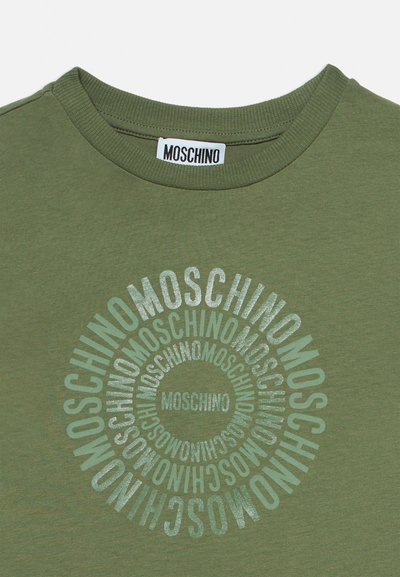 Olívazöld kereknyakú póló, amelynek elején a "MOSCHINO" felirat ismétlődik koncentrikus körökben, és egy Moschino címke található a nyakánál.