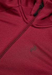 Felpa con zip color marrone bordeaux in tessuto liscio, con una cerniera nera e un logo discreto sul petto. Nessun motivo o dettaglio distintivo visibile.