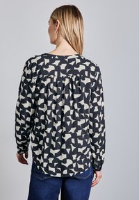 Blusa a maniche lunghe in tessuto nero e crema, con un motivo geometrico astratto, scollatura tonda e dettaglio arricciato sul retro.