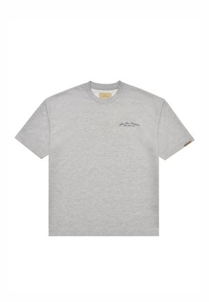 Camiseta gris clara de manga corta con cuello redondo, con pequeño texto negro en el lado izquierdo del pecho y una pequeña etiqueta de tela en la manga izquierda.