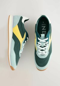 Sneaker sportive verde e gialle con tomaia in suede e pelle, dotate di lacci bianchi, suola in gomma e design della punta arrotondato.