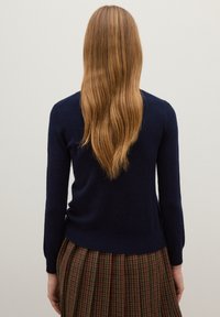 Marineblauer, langärmeliger Pullover aus weichem Material mit taillierter Passform, kombiniert mit einem plissierten Rock im braun-grünen Karomuster.