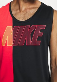 Haut sans manches Nike, moitié rouge et moitié noir, avec un grand logo en dégradé rouge et jaune. Confectionné dans un tissu léger au toucher lisse.