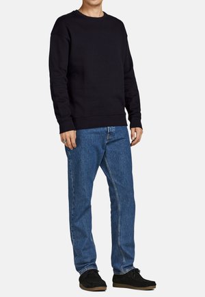 Svart bomullströja med ribbstickade ärmar och nederkant, kombinerad med ljusblå denimjeans. Skorna är i svart mocka med gummisula.
