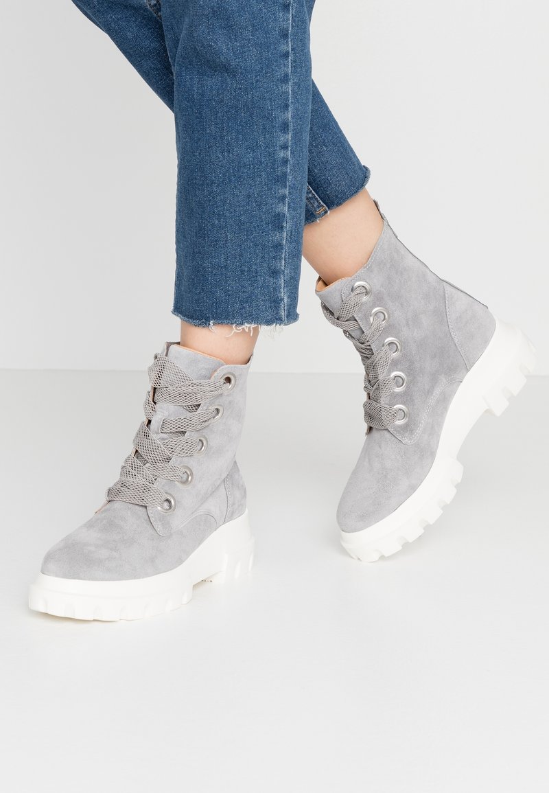 Stivaletti alla caviglia in suede grigio con suola in gomma bianca spessa, dotati di lacci in rete grigia e occhielli in metallo, abbinati a jeans di denim a vita corta.