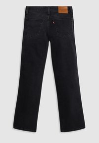Jeans anchos negros de mezclilla, con un parche de cuero en la cintura, bolsillos traseros y un acabado limpio.